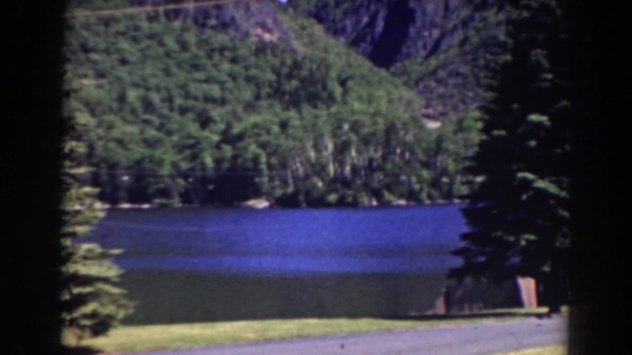 Blue lake below green hills, with evergreen trees at the right edge.