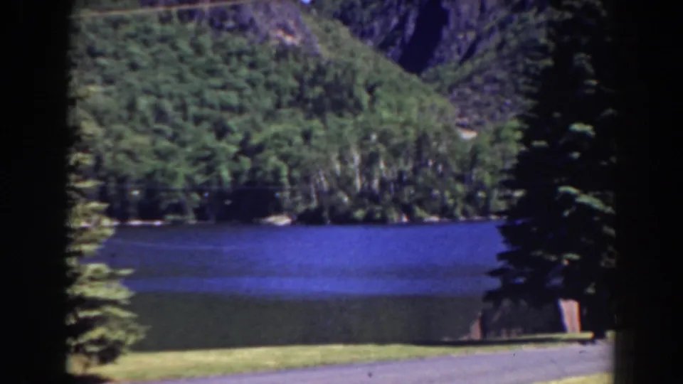 1938 Mount Washington-area landscape with a blue lake, wooded hills, rocky slopes, clear sky, and dark 8mm frame edges.