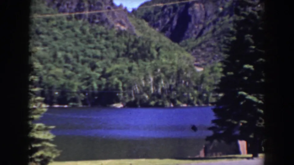 1938 Mount Washington-area 8mm view of a lake bordered by dense trees, steep hills, and dark film gate edges.