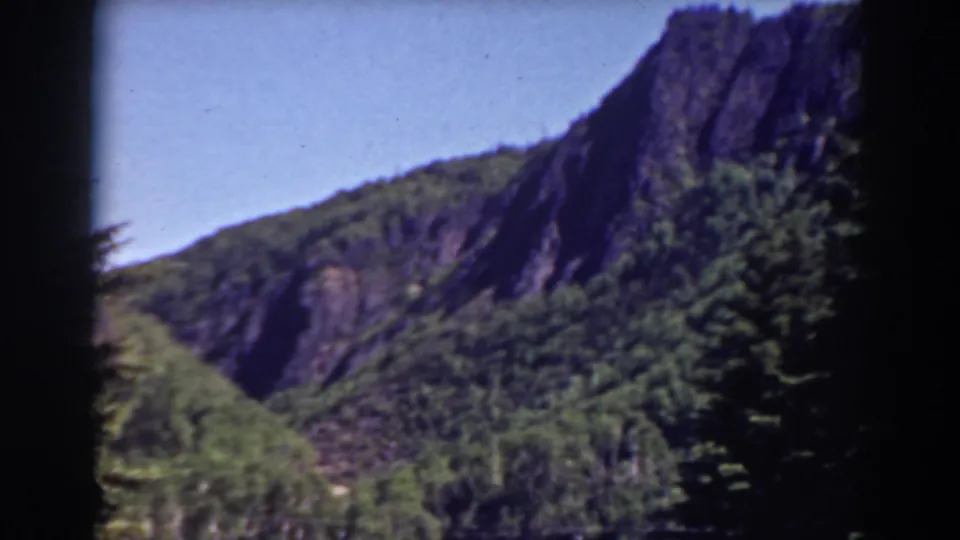 Mount Washington-area 8mm frame with steep rock faces, green wooded slopes, open sky, and pronounced dark edge shadowing.