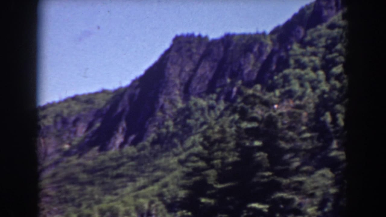 Mount Washington landscape with a rugged ridge, wooded hillside, blue sky, and visible 8mm frame borders from the 1938 home movie.