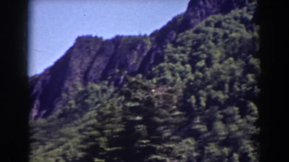1938 Mount Washington footage showing a tree-covered slope, exposed dark cliffs, and handheld 8mm framing in a scenic mountain view.