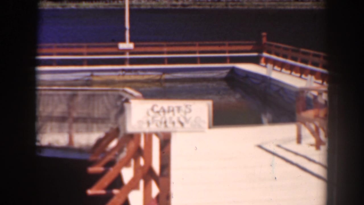 Wooden dock with railings and a painted sign reading CAPT'S FOLLY beside calm water.