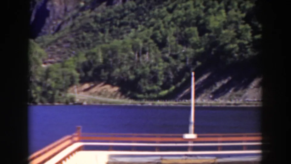 Mount Washington, New Hampshire 8mm frame with a dock post and railing in front of still water, forested shore, and steep rocky hillside.