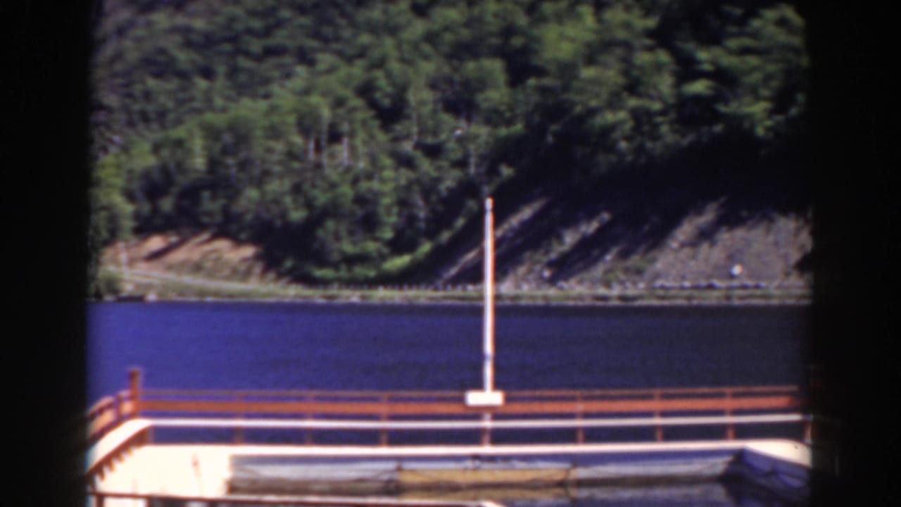1938 8mm view associated with Mount Washington, New Hampshire, showing a dock railing, blue water and wooded rocky shore.