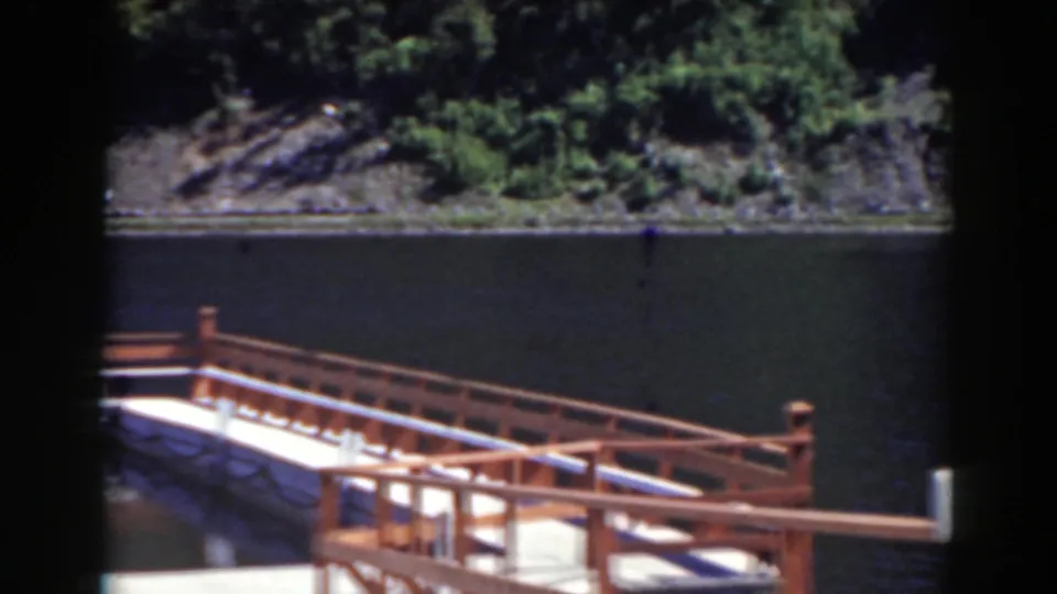 Mount Washington, New Hampshire home-movie frame showing an angled dock railing, still water and a wooded shoreline.