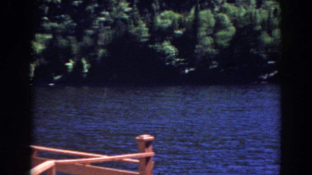 Blue lake seen beyond a reddish wooden railing with forested shoreline in the background.