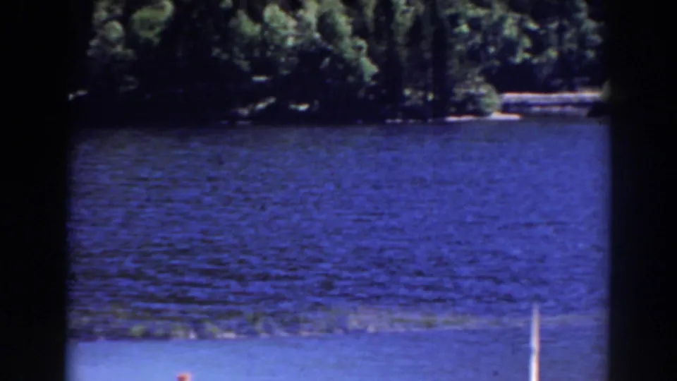 Mount Washington, New Hampshire home-movie frame showing blue lake water, distant trees, and a pale vertical post near the lower edge.