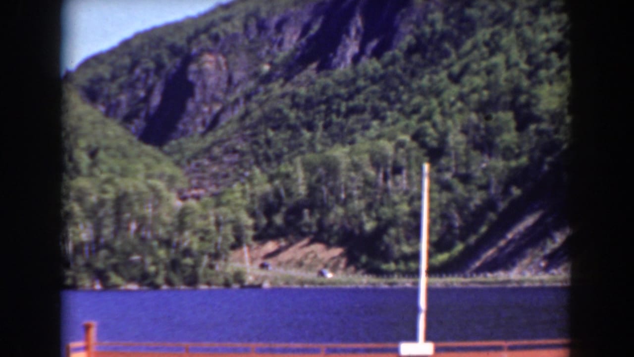 Blue lake with wooded rocky slopes, a railing, and a white pole in the foreground.