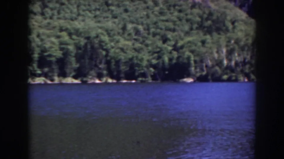 Home-movie landscape frame of blue lake water and a wooded shoreline, with strong 8mm border and contact-sheet division visible.