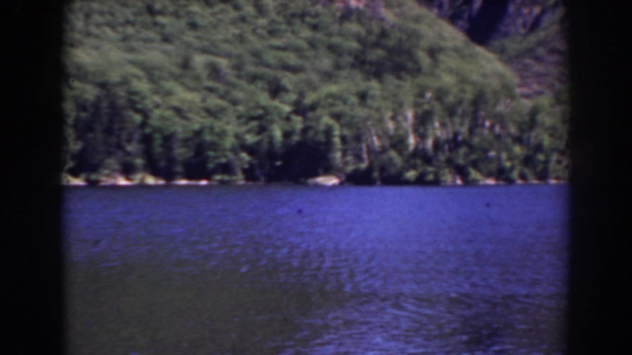 Blue mountain lake with forested slopes and dark film gate edges.