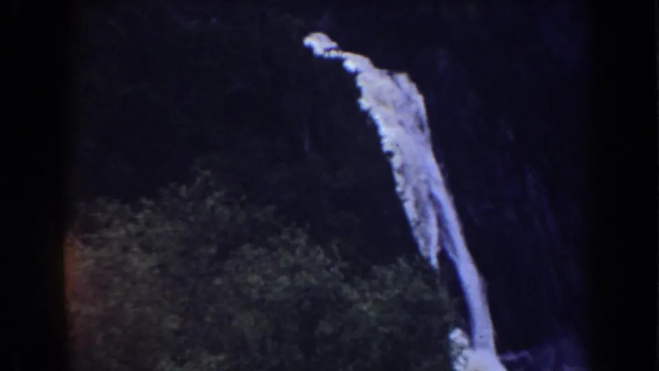 Archival 8mm view of a waterfall in the Mount Washington, New Hampshire area, framed by dark rock and dense vegetation.