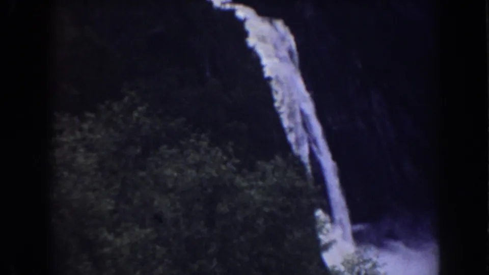 1938 home-movie frame showing a tilted view of a narrow waterfall dropping beside thick greenery in New Hampshire mountain terrain.