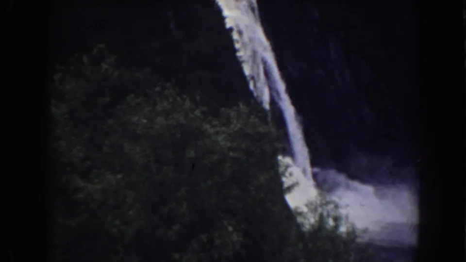 1938 Mount Washington-area 8mm frame showing a narrow waterfall, shadowed cliff, green trees, and pale mist near the base.