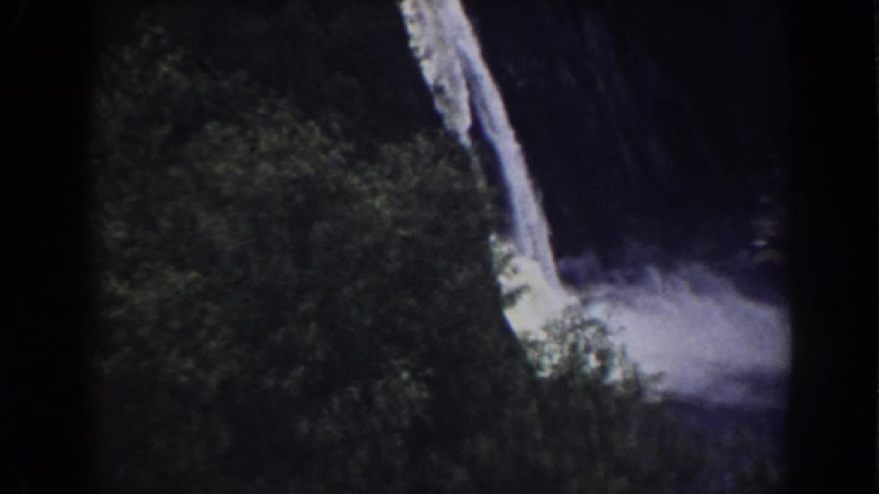 1938 Mount Washington-area frame with a bright falling stream, green foliage, dark cliff shadows, and mist spreading at the base.