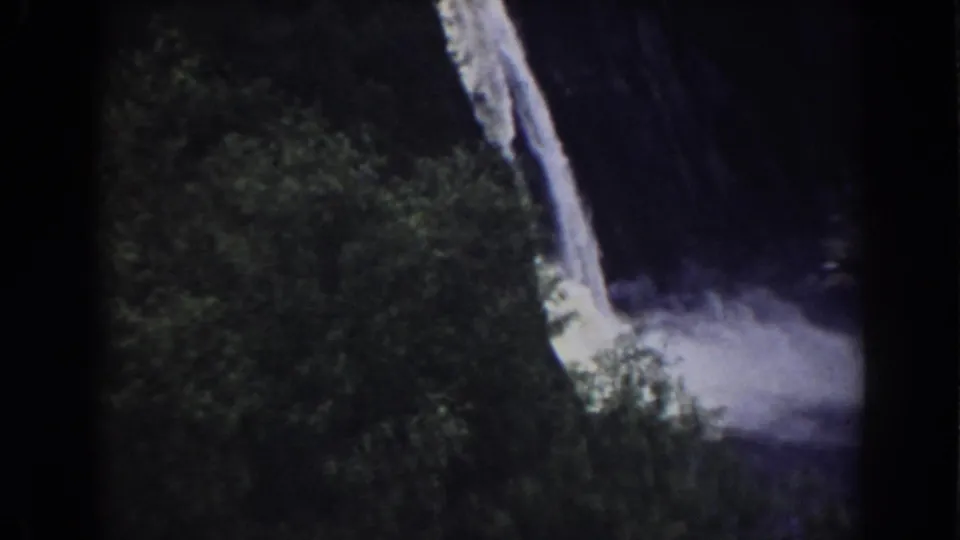 1938 Mount Washington-area frame with a bright falling stream, green foliage, dark cliff shadows, and mist spreading at the base.