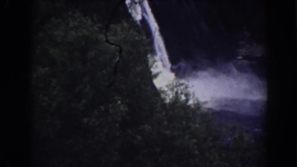 1938 Mount Washington-area 8mm frame showing foliage in the foreground and a pale waterfall descending into blue-purple mist.