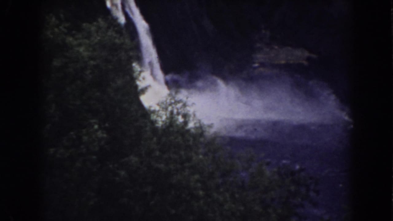Waterfall dropping beside dark foliage into a misty pool.