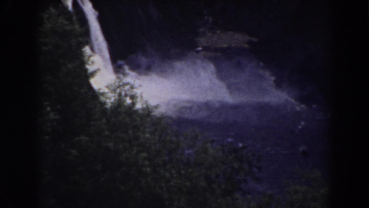 Bright waterfall and spray over a dark lagoon bordered by trees.