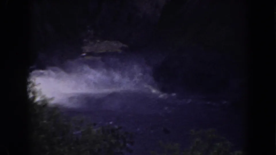 Late frame shows the waterfall partly low in view, with heavy spray spreading over the dark lagoon and surrounding trees.