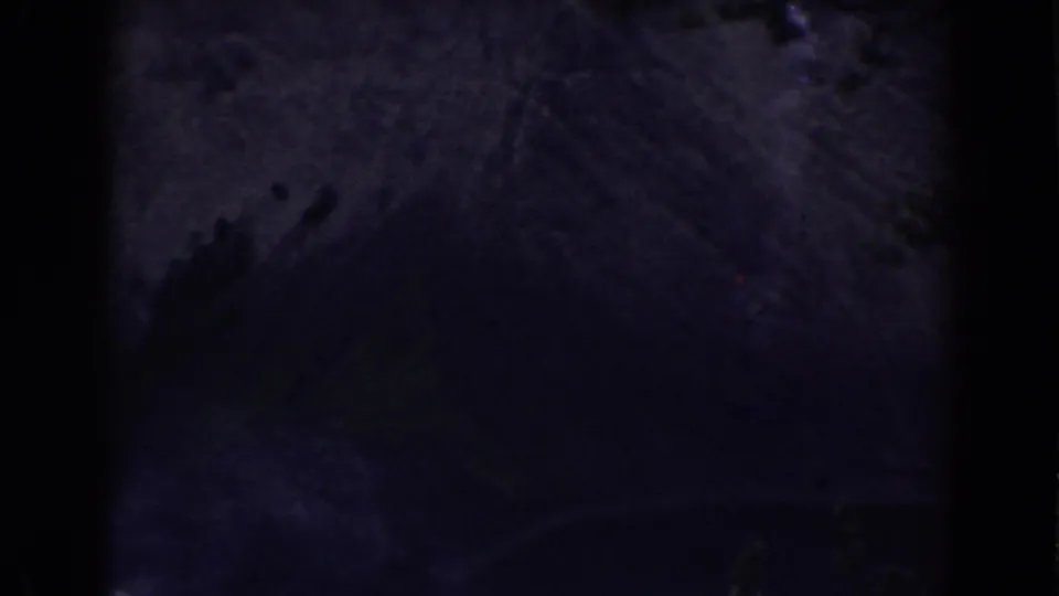 The 1938 home-movie frame appears to show rocky terrain beside dark water, with strong grain and low-light exposure.