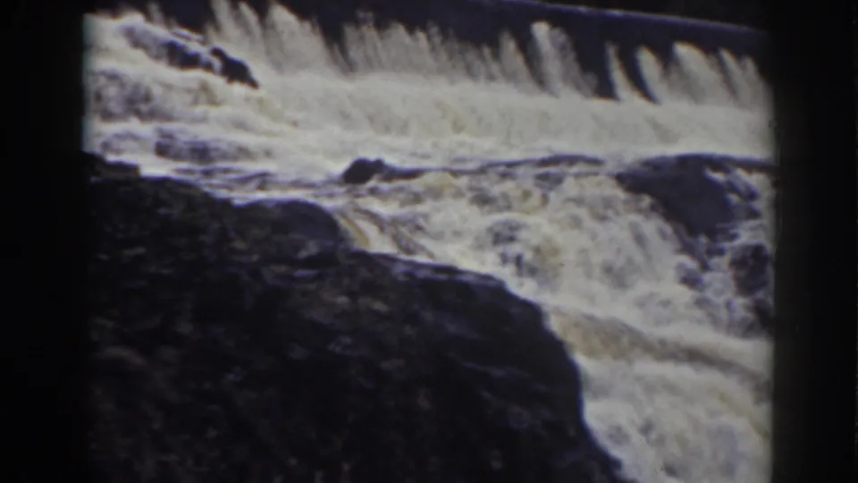 1938 Mount Washington home-movie frame with white water, dark rocks, and pine branches crossing the top edge.