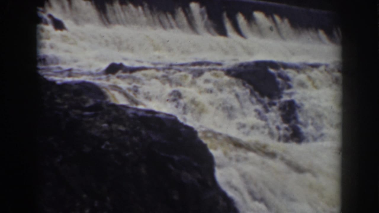 Foaming waterfall current spilling over dark rocks with black film borders.