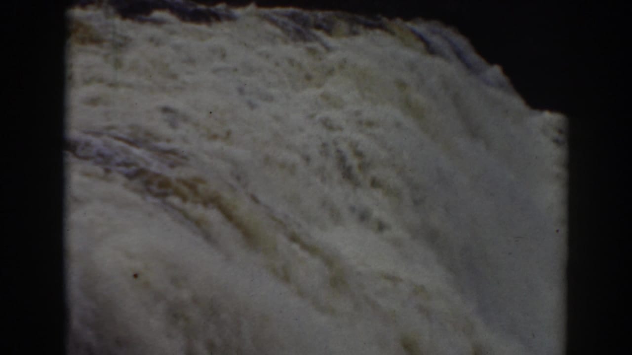 Late-clip 8mm frame of Mount Washington falls water sweeping past a dark rock edge, with visible film border.