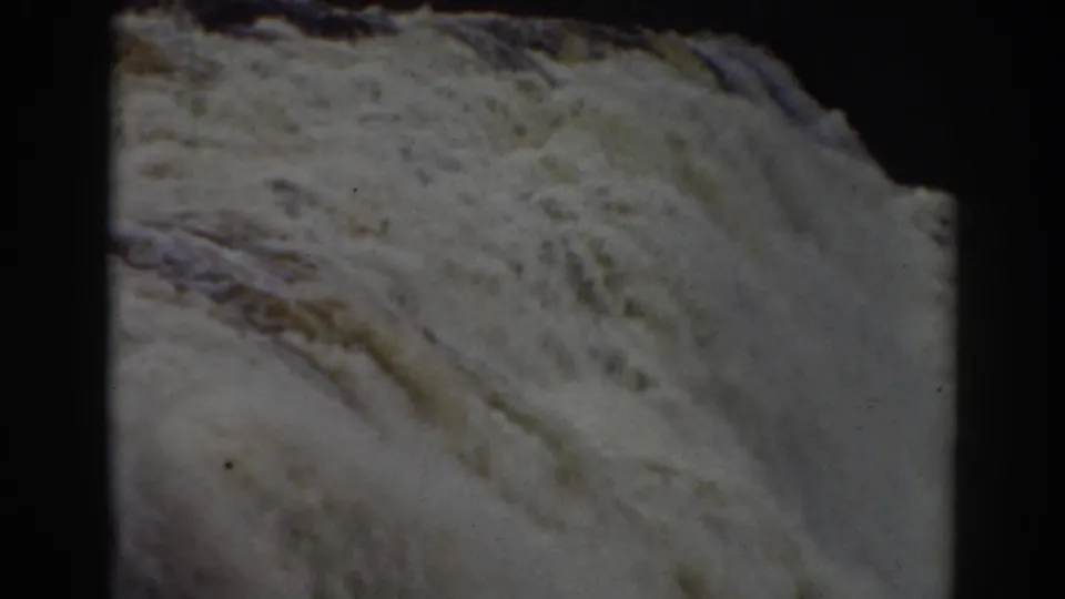 Late-clip 8mm frame of Mount Washington falls water sweeping past a dark rock edge, with visible film border.