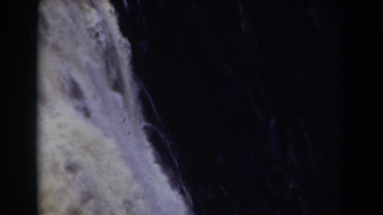 Mount Washington area waterfall detail showing white water beside a dark vertical rock channel, recorded with grainy 8mm home-movie texture.