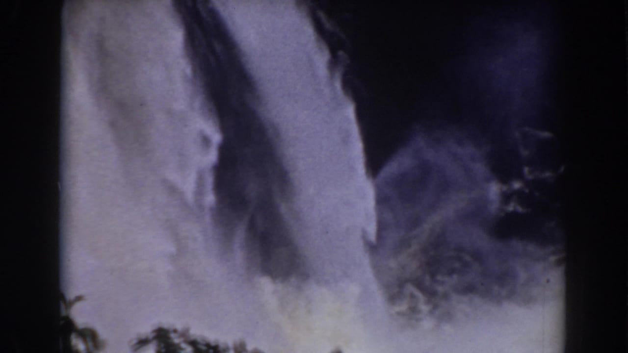 Vintage 8mm frame of the Mount Washington waterfall with mist rising above dark green foliage.