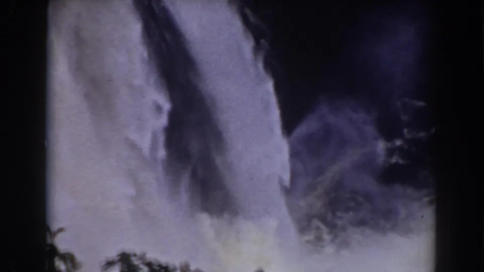 Vintage 8mm frame of the Mount Washington waterfall with mist rising above dark green foliage.