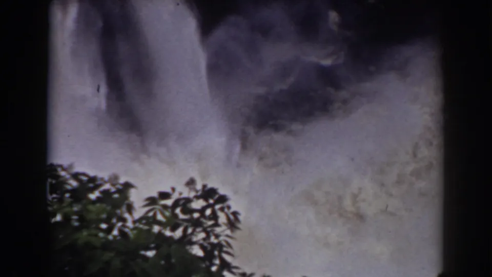 1938 Mount Washington home-movie frame showing waterfall spray behind silhouetted tree branches and dark film borders.