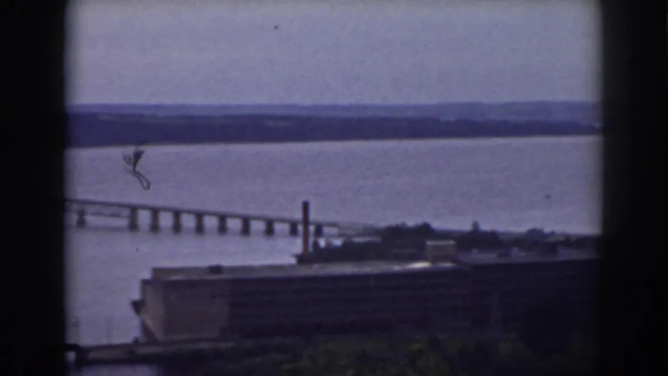 1938 8mm view of a long bridge over a broad river near Mount Washington, New Hampshire, seen through dark window framing.