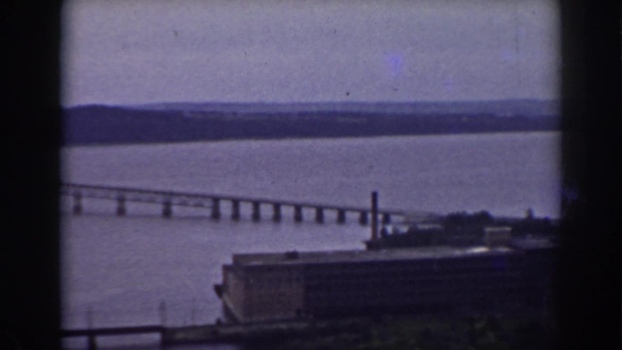 Long river bridge and distant shore are visible through a dark window frame in this 1938 New Hampshire home-movie frame.