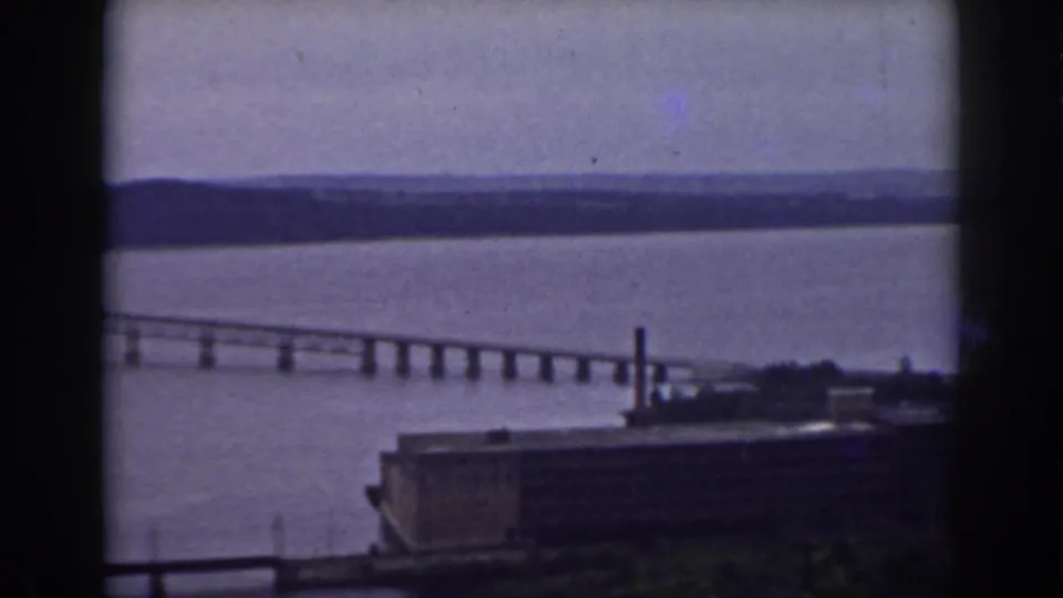 Long river bridge and distant shore are visible through a dark window frame in this 1938 New Hampshire home-movie frame.