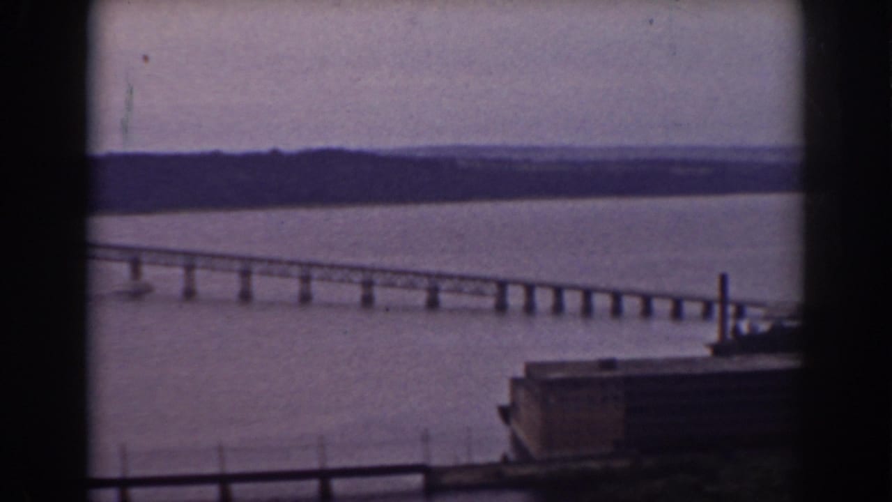 Long bridge crossing a wide lake, seen through dark window framing.