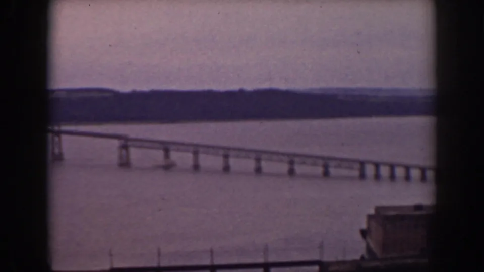 Soft 8mm frame of a long bridge crossing a lake in New Hampshire, partly obscured by the window framing.