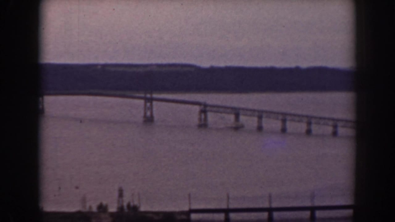 A long bridge stretches across the water in this 1938 Mount Washington, New Hampshire home-movie frame, partially bordered by window framing.