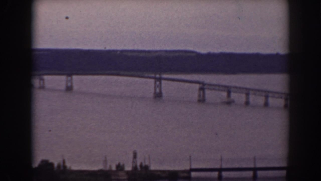 Vintage 8mm frame showing a bridge span over broad water near Mount Washington, New Hampshire, with distant woods and window-edge framing.