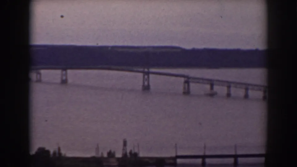 Vintage 8mm frame showing a bridge span over broad water near Mount Washington, New Hampshire, with distant woods and window-edge framing.