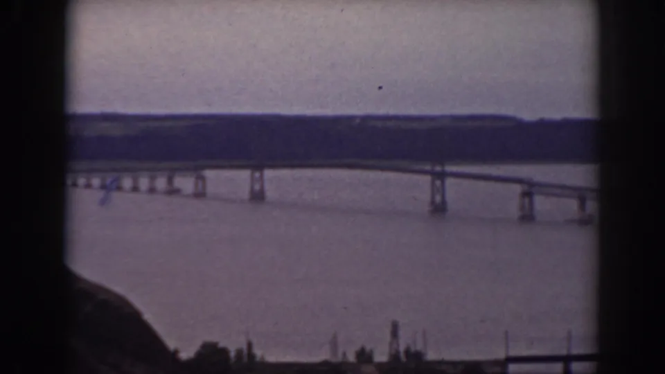 1938 New Hampshire home-movie frame showing a long bridge over water from an elevated rocky vantage point.