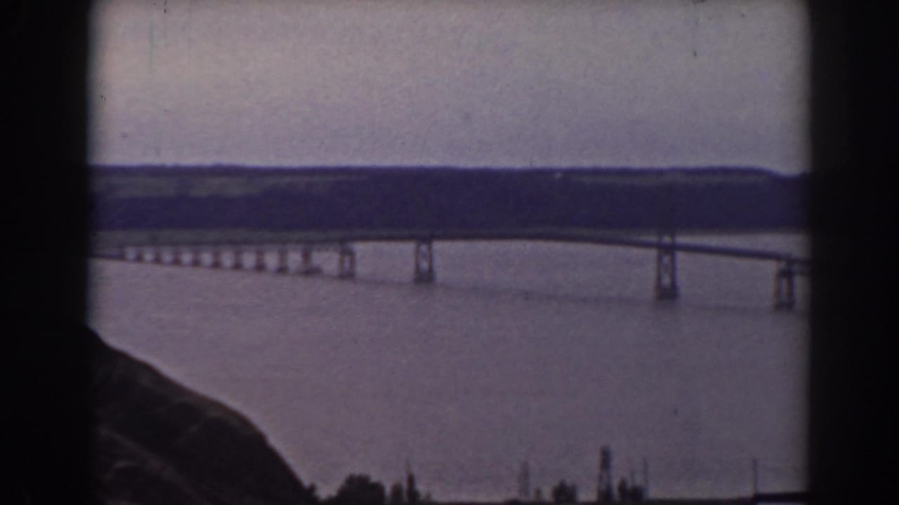 Elevated 1938 view in New Hampshire of a bridge crossing a broad body of water, framed by hillside and distant ridgeline.