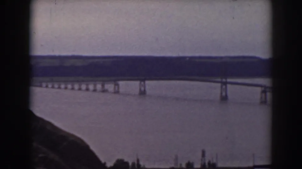 Elevated 1938 view in New Hampshire of a bridge crossing a broad body of water, framed by hillside and distant ridgeline.