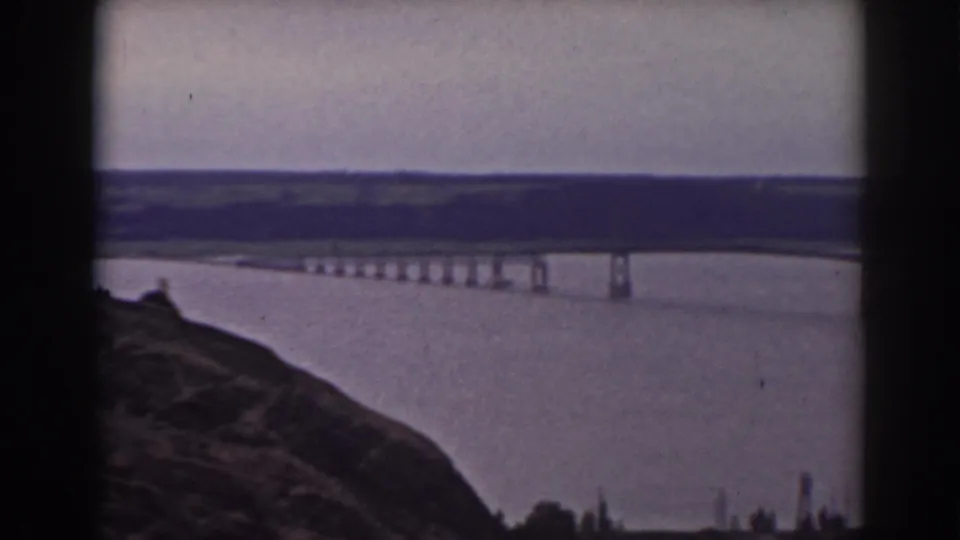 Final 1938 New Hampshire frame of the bridge and water landscape, viewed from a high rocky foreground with distant hills.