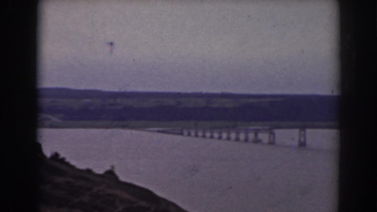 1938 Mount Washington, New Hampshire home-movie frame showing a lake, long bridge, hillside foreground, and distant low hills.