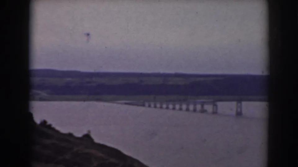 1938 Mount Washington, New Hampshire home-movie frame showing a lake, long bridge, hillside foreground, and distant low hills.