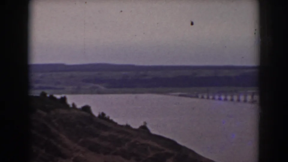 1938 New Hampshire travel frame with a hillside foreground overlooking a lake and a long bridge crossing the water.