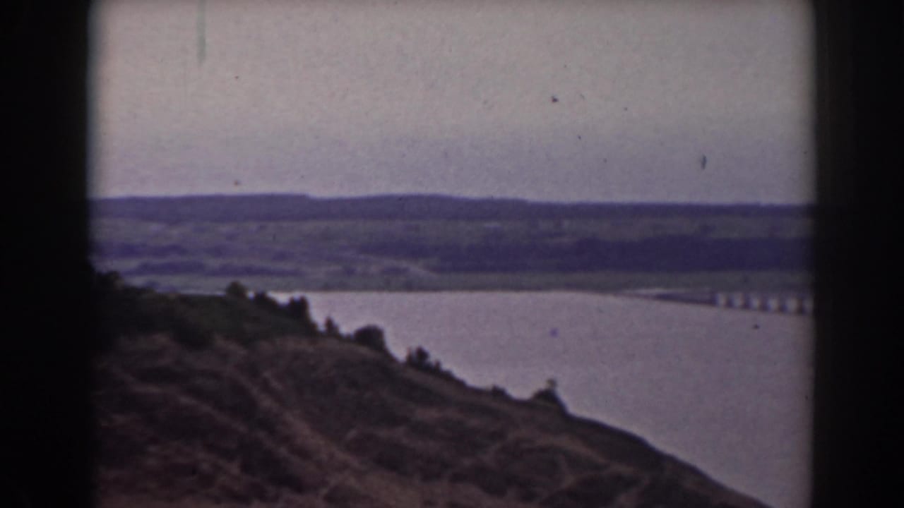 Soft 8mm frame from the 1938 Mount Washington clip, with a wooded slope above a lake and the bridge partly cropped at right.