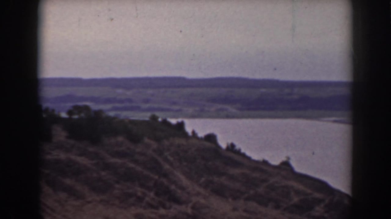 Final 1938 New Hampshire frame showing a hillside foreground, lake water, distant hills, muted sky, and dark 8mm frame edges.